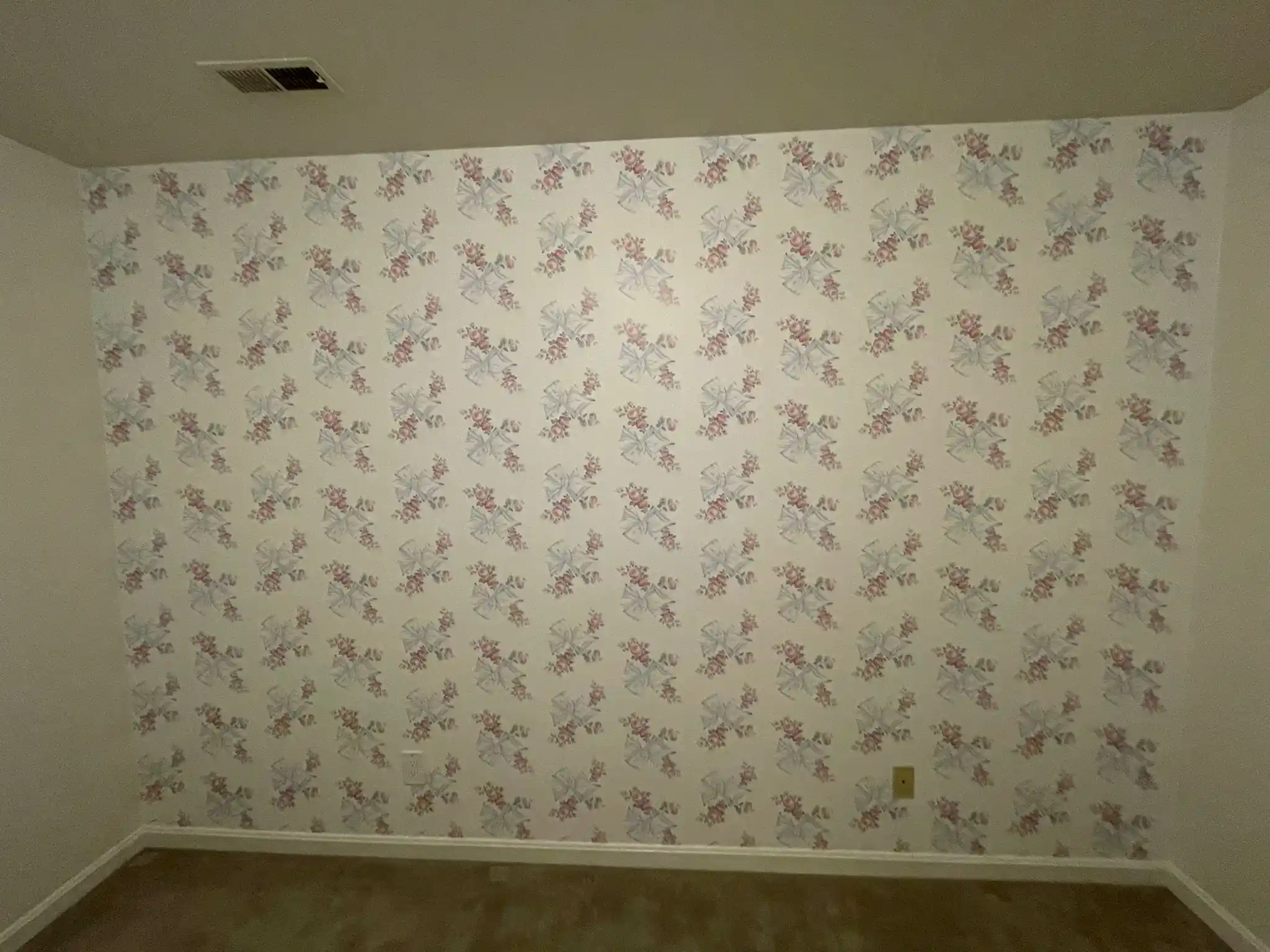An interior wall covered in pale floral wallpaper, shown across its full width